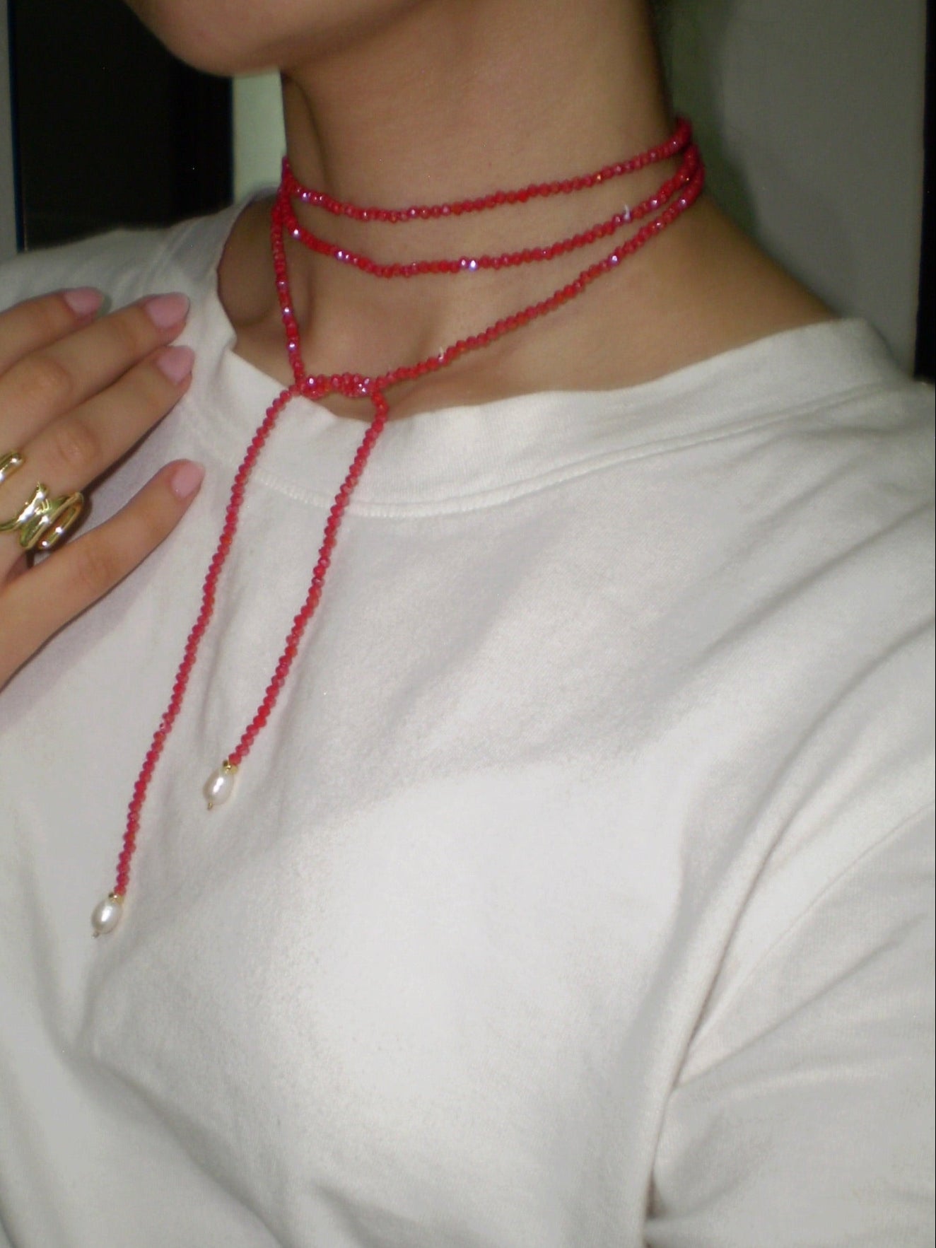 Person wearing a red beaded necklace with a plain background